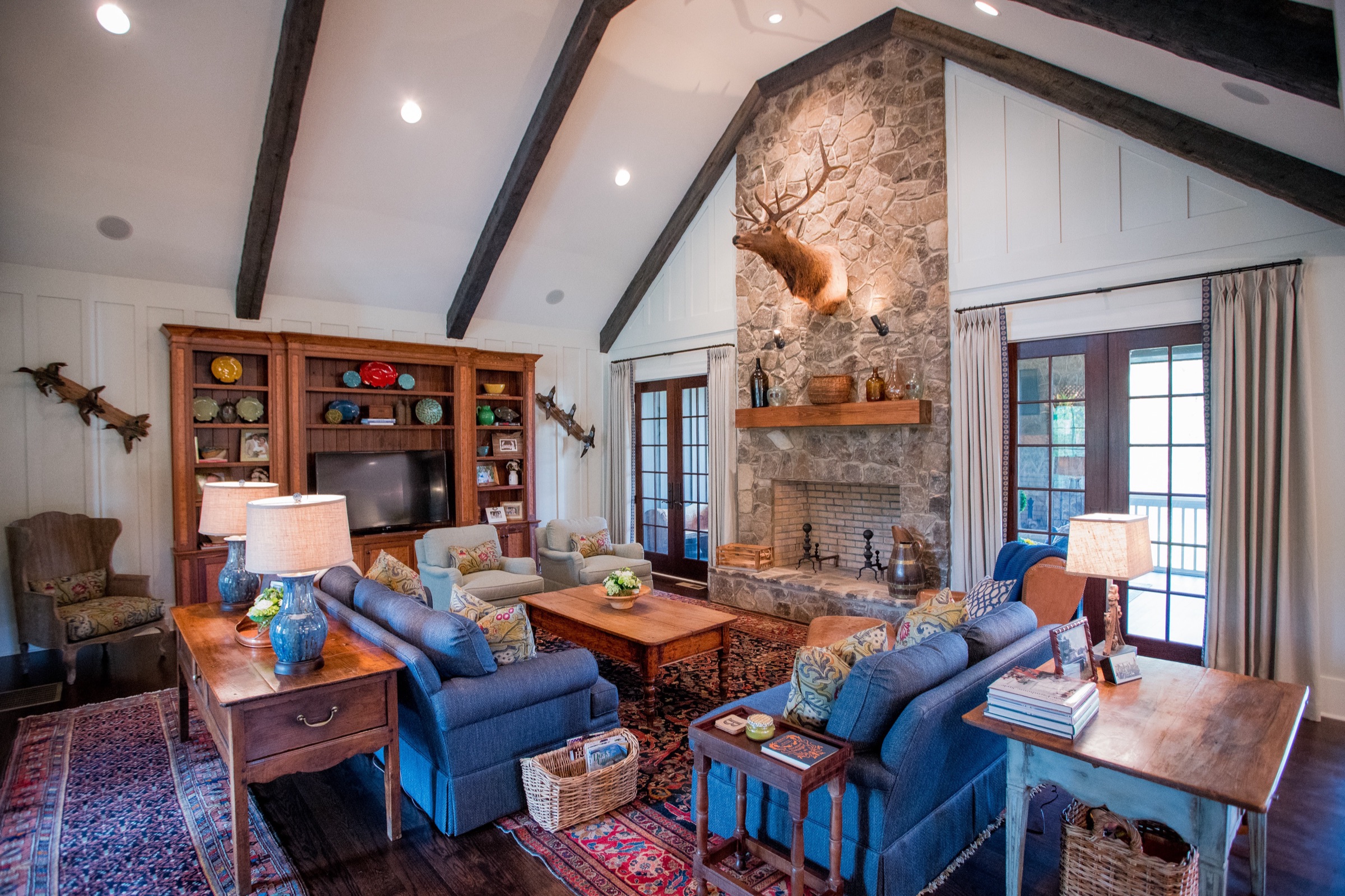 Vaulted great room with timber trusses, stone fireplace, and blue leather seating