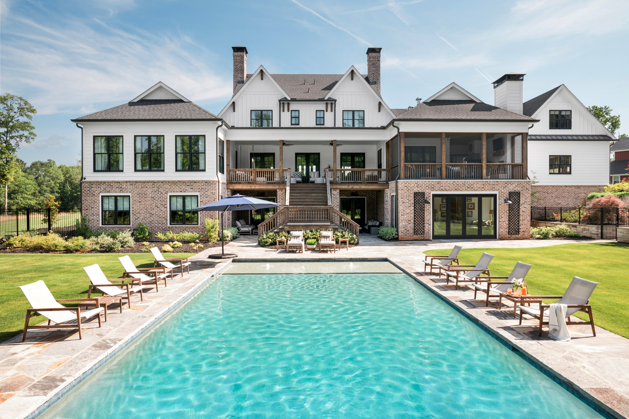 Intown Farm rear elevation with a long pool, stone terrace, and white farmhouse facade