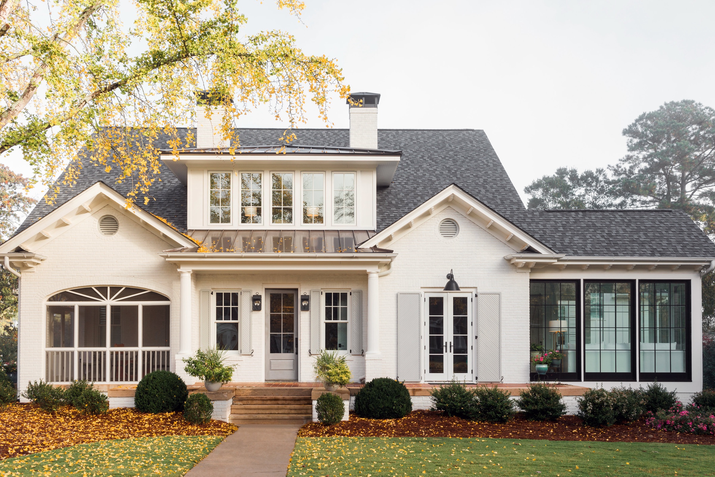 Two-story white traditional home with screened porch and gabled bay, autumn leaves on the lawn