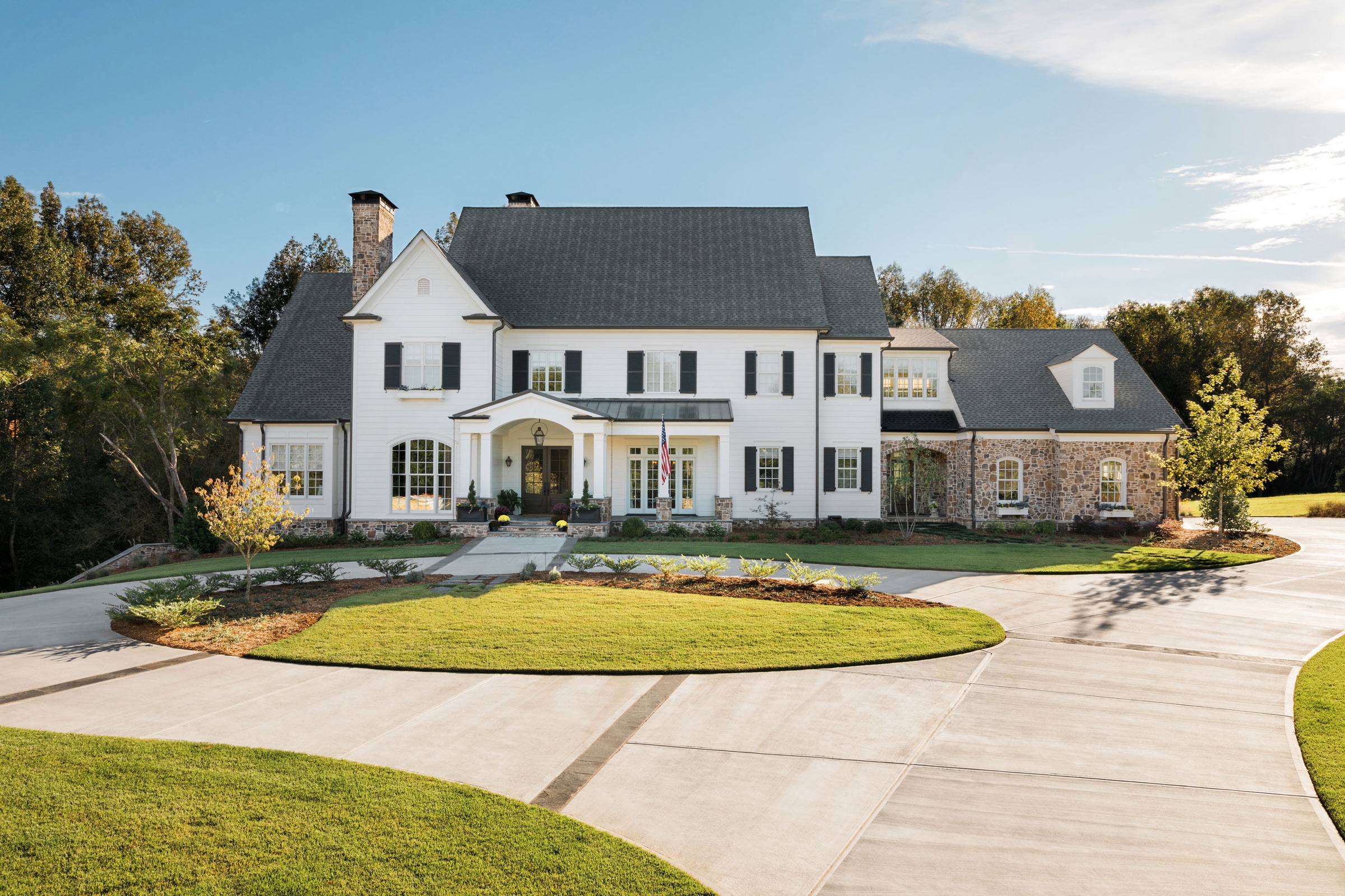 White-and-stone Georgian estate with shuttered windows and circular driveway, late afternoon light